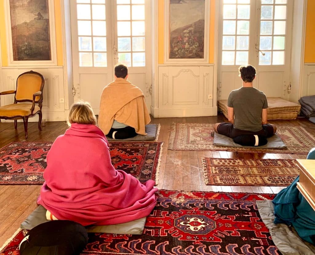 three people meditating in sunny room